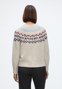 Beežist kootud sviiter, millel on mustriline yoke, kus on punase, sinise ja mustaga zigzagi mustrid; kastikujuline lõige ning soonikkoes äärised ja varrukaotsad.