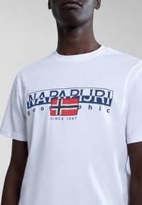 Tricou alb din bumbac, cu un mare logo bleumarin și un grafic cu steagul norvegian. Guler simplu tip crew și mâneci scurte, fără alte modele.