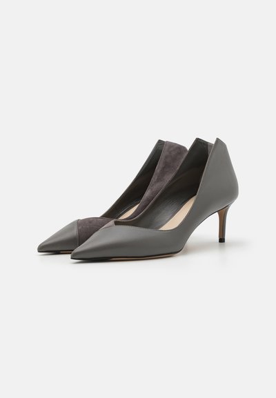 Grå læder- og ruskindspumpe med spidse tæer, åbne sider og en lav stiletto hæl. Har en glat finish og kontrasterende teksturer.