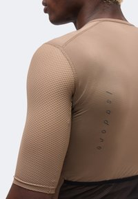 Άνδρας που φοράει μπεζ, υφασμάτινο αθλητικό κοντομάνικο μπλουζάκι με το «Isadore» τυπωμένο κάθετα στην πλάτη.