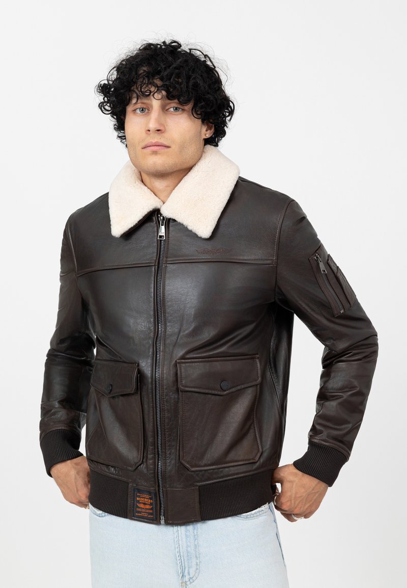 Bruin leren jack met een crèmekleurige schapenvachtkraag, ritssluiting, twee voorzakken en geribde manchetten. Geweven afwerking en duurzame ontwerp.