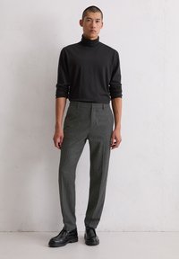 Zwarte coltrui met lange mouwen, gecombineerd met slanke grijze broek met streep en zwarte leren schoenen. Soepele textuur overal.
