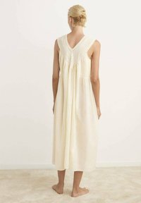 Vestido sin mangas de color amarillo claro, con espalda en forma de V, tejido texturizado y detalle fruncido en la cintura, que llega hasta la mitad de la pantorrilla.