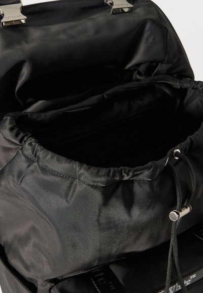 Sac à dos en nylon noir avec fermeture à cordon et ferrures métalliques, montrant le compartiment principal ouvert et la doublure intérieure.