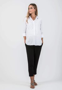 White button-up shirt with long sleeves, paired with black tapered pants and embellished sandals, showcasing a sleek and minimal design.