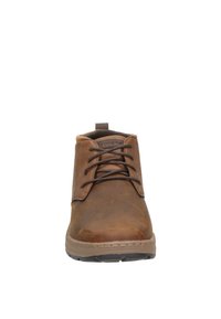 Botas de tobillo de cuero marrón con diseño de cordones, puntera redondeada, suela de goma de color marrón claro y costuras en la parte superior para un detalle adicional.