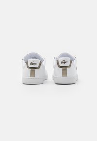 Baskets en cuir blanc à la texture lisse, dotées d'un accent doré sur le talon et d'un patch logo à l'arrière. Design minimaliste.