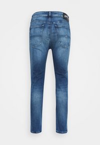Blue denim jeans with back pockets, subtle fading on legs, and a black Tommy Hilfiger brand label on the waistband.
