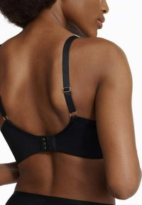 Czarny stanik z regulowanymi ramiączkami, zapięciem na haczyk i oczko, gładkiego materiału oraz z detalami w złotym odcieniu, charakteryzujący się niskim plecami.