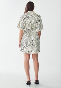 Korte mouw jurk in lichtbeige met zwarte draaiende patronen, met een getailleerde taille en een vloeiende rok, afgewerkt met stiletto hakken.
