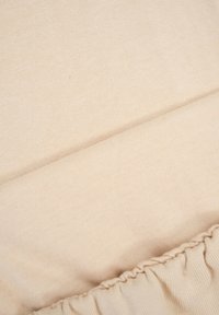 Zbliżenie beżowego materiału tekstylnego z gromadzonym elastycznym brzegiem, ukazujące szczegóły miękkiego dzianinowego materiału.