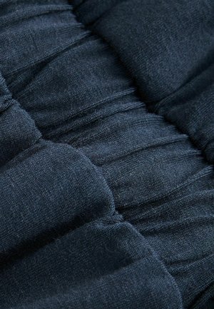 Tmavě modrá polstrovaná tkanina s texturovaným povrchem, s nařasenými částmi a jemnými švy, což vytváří prostorový vzhled.