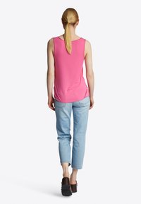 Top rosa smanicato con vestibilità ampia, scollatura a girocollo, spacchi laterali; abbinato a jeans tapered blu chiaro e scarpe con plateau marroni.