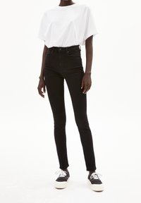 Jeans skinnies negros de talle alto con una textura suave, combinados con una camiseta blanca holgada y zapatillas negras con suela gruesa y cordones.