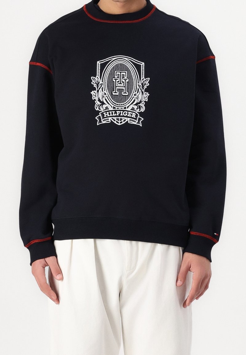 Sudadera de la Marina con acentos rojos y emblema blanco que presenta el texto "Hilfiger". Puños y cuello acanalados, tela suave, ajuste relajado.