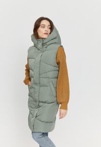 Green padded vest with a high collar, zip closure, and side pockets. Features quilted texture and a knee-length design. Casual fit.