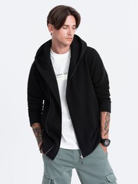 Zwarte zip-up hoodie met een grote capuchon, een textuurstof en geribde manchetten, over een wit T-shirt gedragen. Model draagt groene cargobroek.