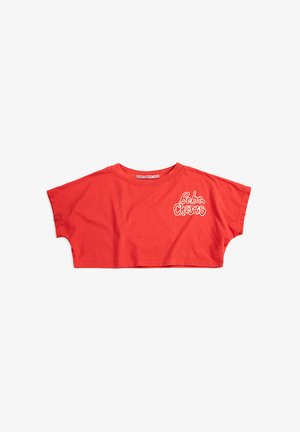 T-shirt rouge court à manches courtes avec col rond et texte blanc "Bobo Choses" sur la poitrine gauche, posé à plat sur fond blanc.