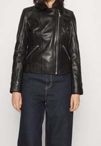 Zwarte leren cropped jas met een rits aan de voorkant, zijzakken en een kraag van bruin fleece. Gecombineerd met donkere denim wijde broek.