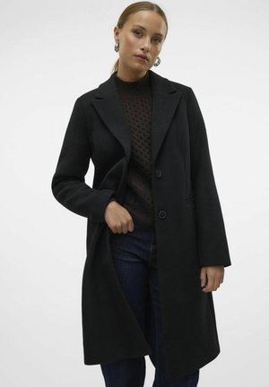 Zwarte wollen blend jas met een notch lapel, twee knopen en zijzakken. Draagt over een donkere trui en blauwe spijkerbroeken. Gladde textuur.