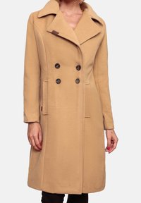 Beige wollen jas met een dubbele rij knopen, brede revers, zwarte knopen, zijzakken en een knie-lange silhoeët.
