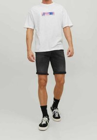 Camiseta blanca con un estampado gráfico colorido, combinada con pantalones cortos de denim negros doblados en el dobladillo. Zapatillas negras con suelas blancas.