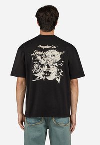 Sort bomulds t-shirt med et stort hvidt blomstermotiv og tekst på ryggen. Løs pasform og korteærmer. Rund halsudskæring.