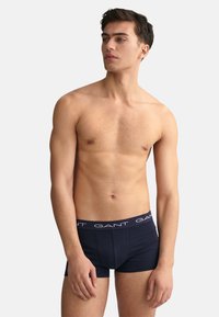 Boxeri de culoare bleu marin, cu o textură solidă și un brâu elastic, având logo-ul alb "GANT". Modelul pozează pe un fundal neutru.