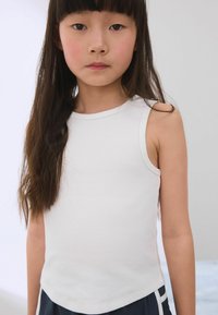 Witte geribbelde mouwloze top met een ronde halslijn, onopgesmukte zijden en een gladde textuur, gecombineerd met donkere sportieve shorts.