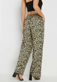 Byxdress med leopardmönster i lätt tyg, med resår i midjan, två sidofickor och en neutral beige bakgrund.
