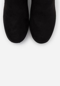 Botines de ante negro con punta redondeada y textura suave. Presentan un acabado liso y costuras sutiles a lo largo de los bordes.