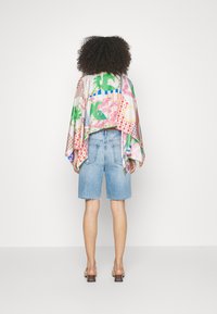 Capa de seda de colores con diseños de palmas verdes y geométricos, combinada con unos pantalones cortos de denim azul con dobladillo deshilachado.