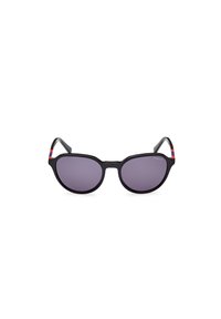 Gafas de sol negras con lentes ovalados y tinte púrpura. Presentan un marco elegante y rayas de color en el borde de las patillas. Nombre de la marca visible.