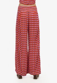 Pantalones de pierna ancha en un vibrante patrón geométrico rojo y rosa. Presentan una cintura fruncida y una tela ligera para mayor comodidad. Elementos de diseño texturizados.