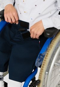 Mörkblå shorts med kardborrestängning och framfickor, tillsammans med en vit randig skjorta. Sedd på en person i en manuell rullstol.