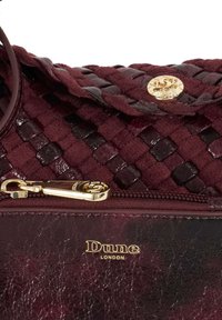 Burgundy handbag made from woven leather and suede, featuring a gold zipper and logo. The design includes a textured finish and an elegant clasp.