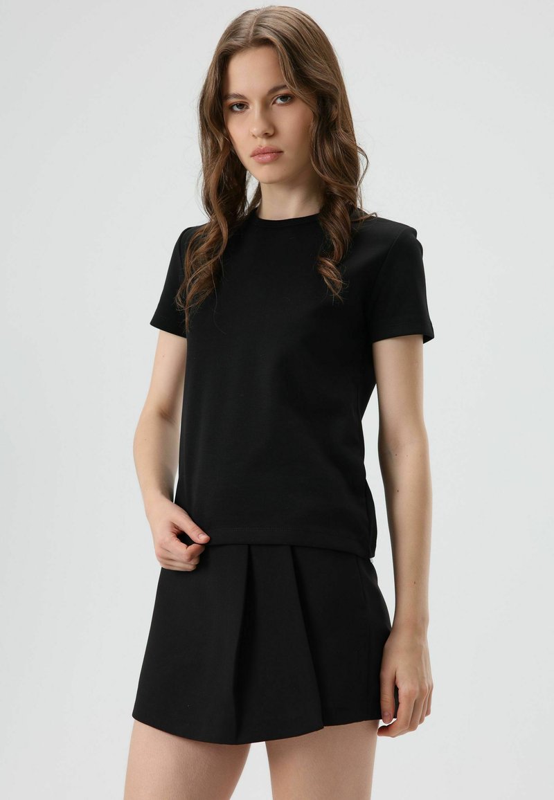 T-shirt noir à manches courtes associé à une mini-jupe plissée noire. Le tissu semble lisse avec une silhouette ajustée et un col rond.