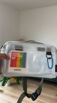 Mala de tirar transparente com exterior texturizado ripstop, alça verde, mosquetão azul e etiqueta colorida com a inscrição "Mala de Tirar Ripstop".