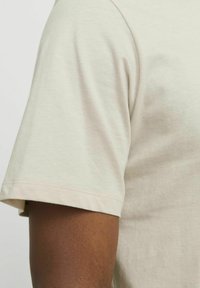 Lichtbeige t-shirt met korte mouwen, gemaakt van zachte katoen, heeft een ronde hals en een gladde textuur met een minimalistisch ontwerp.