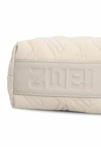 Beige gesteppte Tasche mit glatten, matten Lederakzenten. Verfügt über ein eingeprägtes Logo auf dem Lederfeld und ein sichtbares Nähmuster.