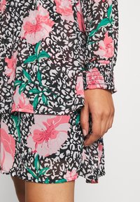 Abito floreale con motivi di fiori rosa e foglie verdi su uno sfondo di stampa leopardata in bianco e nero. Maniche elastiche e dettaglio dell'orlo a strati.