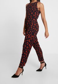 Mono de estampado de leopardo en azul marino con manchas rojas, con escote halter y un lazo en la cintura, combinado con tacones de aguja negros.