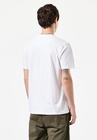Hvid bomulds T-shirt med korte ærmer og rund halsudskæring, båret med olivengrønne bukser. Bagfra ses en subtil tekstur.