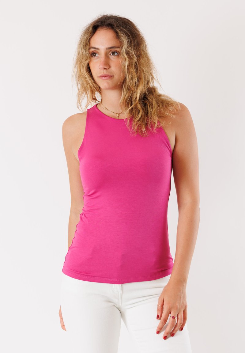 Top a fascia senza maniche in tessuto rosa brillante, caratterizzato da una texture liscia e un collo rotondo, abbinato a pantaloni bianchi per creare un contrasto.