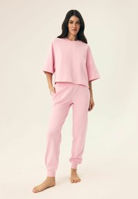 Jasnoróżowy krótki t-shirt z szerokimi rękawami połączony z dopasowanymi joggerami, wykonanymi z miękkiego materiału, z bocznymi kieszeniami i elastycznymi mankietami.