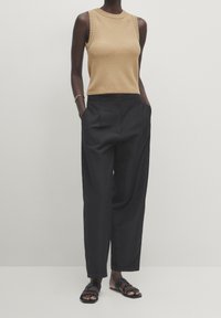 Tan ribbed ilmanhiha toppi yhdistettynä väljiin mustiin housuihin. Jalkineet koostuvat kudotuista mustista sandaaleista. Yksinkertainen ja minimalistischinen muotoilu.