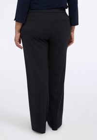 Pantalones de pierna ancha negros con un acabado texturizado, cintura elástica y dos bolsillos traseros. La tela es suave con un sutil patrón.