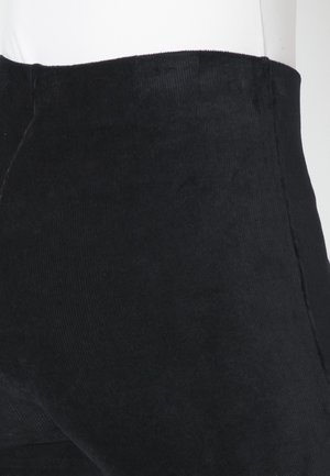 Zwarte ribfluwelen broek met een gestructureerde oppervlakte, slim fit, hoge tailleband en een verticale ribbels patroon, gezien vanuit een zijaanzicht.