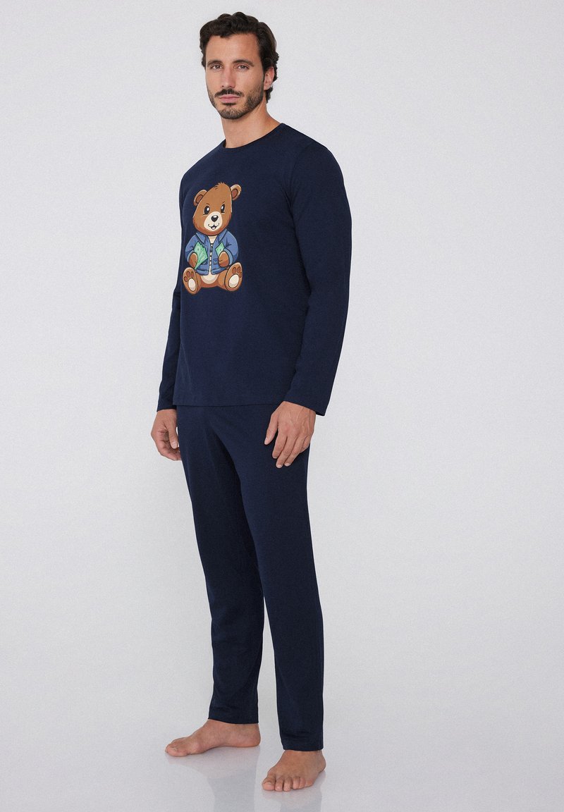 Conjunto de pijama azul marino, con top de manga larga que presenta un gráfico de un oso, combinado con pantalones a juego. Hecho de una tela suave, diseño cómodo.