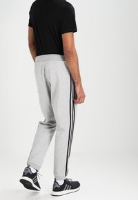 Grå sweatpants har svarta sidostråk, elastisk midja och en tapered ben-design. De är kombinerade med svarta sportskor.